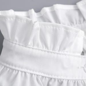 May include: Close-up of a white blouse collar with a ruffled edge. The collar is made of a crisp, lightweight fabric and features delicate stitching. A single white button is visible, adding a touch of detail to the design.