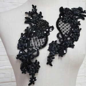 May include: Two black lace appliques with floral designs and sequins. The appliques are on a white background.