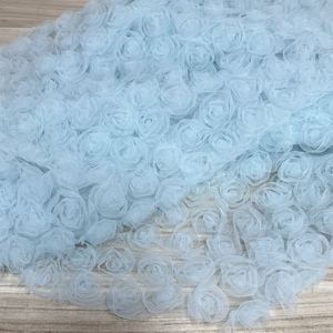 May include: Light blue tulle fabric with a 3D rose design. The fabric is soft and delicate, and the roses are realistic looking.