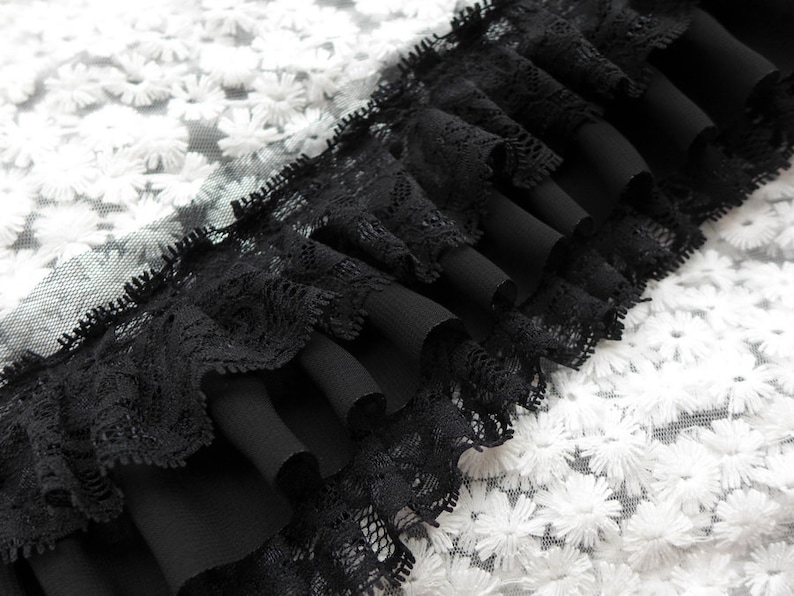 May include: Black lace trim with a ruffled edge, layered over a white fabric with a floral pattern.