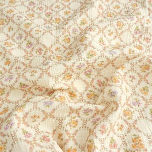 May include: Cream-colored fabric with a repeating floral pattern. The design features small flowers in shades of pink, yellow, and purple, arranged within a lattice of interconnected circles. The fabric has a slightly textured appearance.