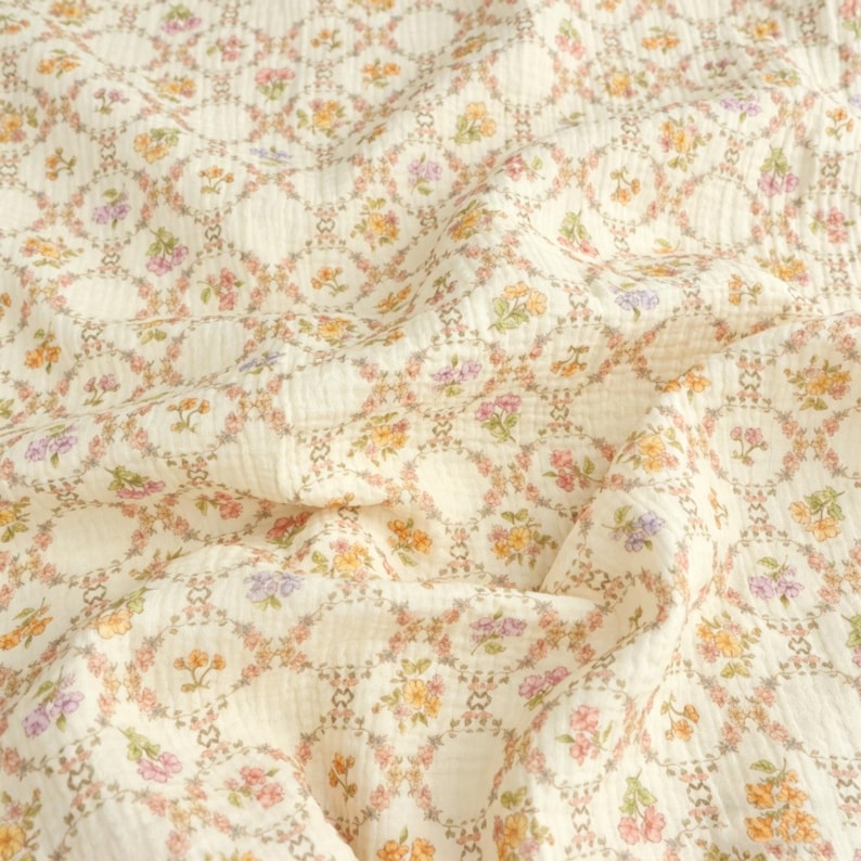 May include: Cream-colored fabric with a repeating floral pattern. The design features small flowers in shades of pink, yellow, and purple, arranged within a lattice of interconnected circles. The fabric has a slightly textured appearance.