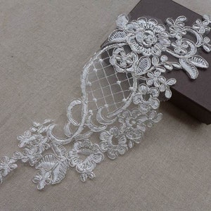 Peut inclure: Garniture en dentelle blanche avec un motif floral. La dentelle est délicate et complexe, avec un fond en maille. Cette garniture est parfaite pour ajouter une touche d'élégance à tout projet.