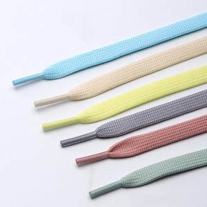 Puede incluir: Un conjunto de seis cordones planos dispuestos en diagonal, con una variedad de colores pastel que incluyen azul claro, crema, amarillo pálido, gris, rosa viejo y verde salvia. Cada cordón tiene una textura tejida suave y una punta de plástico a juego.