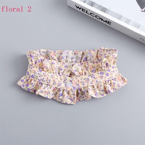 May include: A floral collar with a ruffled edge. The collar is cream-colored with a pattern of small purple and pink flowers. It has a single button closure. The text "floral 2" is in the upper left corner.