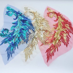 May include: Three sequined fabric appliques in the shape of a stylized bird with a long tail. The appliques are on a sheer fabric background. The appliques are turquoise, gold, and red.