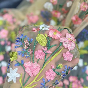 May include: Beige sheer fabric with colorful embroidered flowers. The flowers are pink, yellow, green, blue, and white.