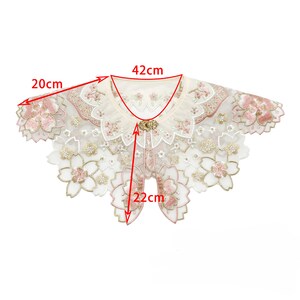 May include: A white lace collar with pink floral embroidery and a gold button detail. The collar measures 42 cm wide and 22 cm long.