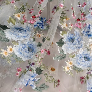 Puede incluir: Tela blanca transparente con dise&ntilde;os florales bordados. Las flores son azules, rosas y verdes. La tela tiene una sensaci&oacute;n delicada y aireada.