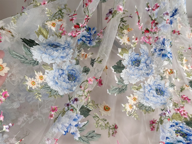 Puede incluir: Tela blanca transparente con dise&ntilde;os florales bordados. Las flores son azules, rosas y verdes. La tela tiene una sensaci&oacute;n delicada y aireada.