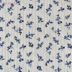 May include: Close-up of a white fabric with a ribbed texture, adorned with a scattered pattern of small blue floral designs. The words "Blue flowers" are visible in the top left corner.