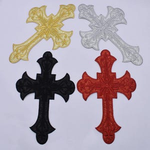 Könnte beinhalten: Vier gestickte Kreuz-Patches in Gold, Silber, Schwarz und Rot. Jedes Kreuz hat ein verziertes Design mit Glitzerakzenten. Die Patches dienen wahrscheinlich dekorativen Zwecken, wie z. B. zum Verzieren von Kleidung oder Accessoires.