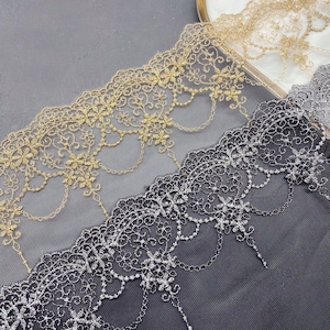 May include: Two pieces of delicate lace trim, one gold and one silver, with intricate floral patterns. The lace is on a black background.
