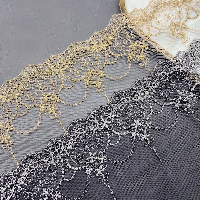 May include: Two pieces of delicate lace trim, one gold and one silver, with intricate floral patterns. The lace is on a black background.