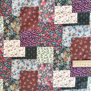 Puede incluir: Una tela de patchwork con varios patrones florales en tonos rojo, azul, amarillo, morado y verde. Una regla de madera es visible en la esquina inferior derecha, mostrando una medida de 15 cm a lo ancho de la secci&oacute;n de tela.