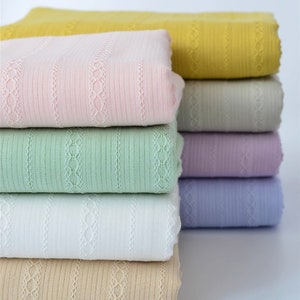 May include: A stack of eight fabric swatches in various colors, including yellow, pink, green, white, beige, gray, lavender, and light blue. The fabric has a striped pattern with a delicate lace design.