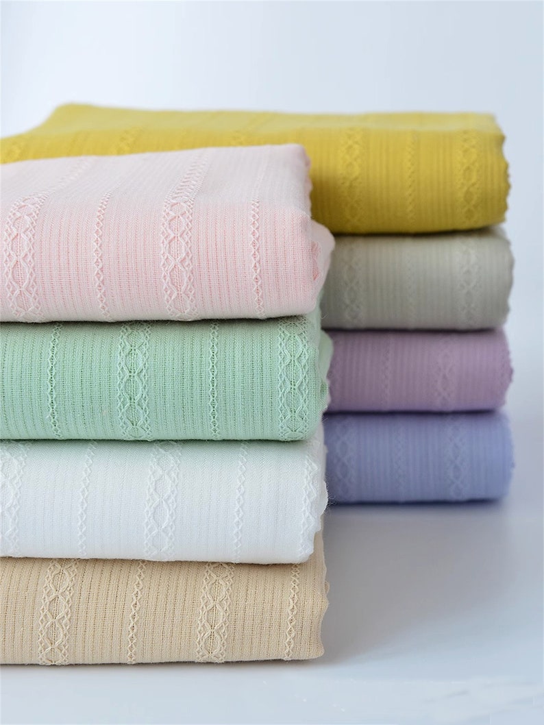 May include: A stack of eight fabric swatches in various colors, including yellow, pink, green, white, beige, gray, lavender, and light blue. The fabric has a striped pattern with a delicate lace design.