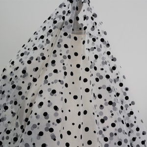 May include: White tulle fabric with black polka dots of varying sizes. The fabric is sheer and has a soft, delicate texture.