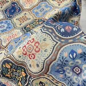 May include: A woven fabric featuring a repeating pattern of interconnected quatrefoil shapes. The design includes floral and geometric motifs in shades of blue, cream, red, and yellow, with a textured surface created by the intricate thread weave.