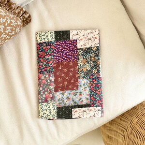 Puede incluir: Un art&iacute;culo de tela rectangular con un dise&ntilde;o de patchwork compuesto por varios patrones florales en tonos rojo, morado, marr&oacute;n, verde, azul y crema. Los cuadrados de tela individuales est&aacute;n cosidos para formar un collage floral multicolor.