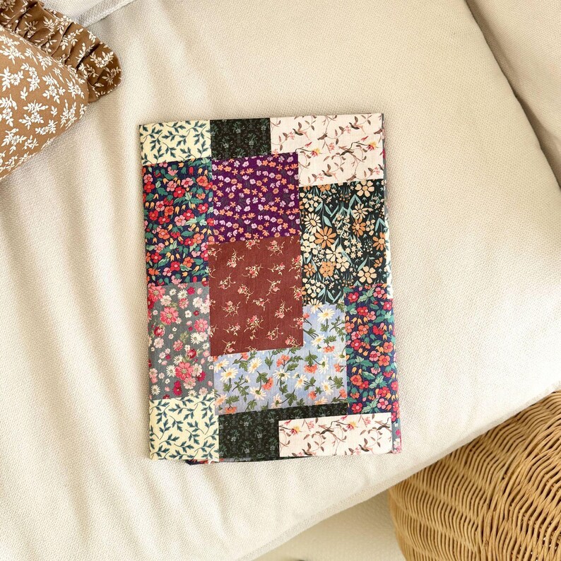 Puede incluir: Un art&iacute;culo de tela rectangular con un dise&ntilde;o de patchwork compuesto por varios patrones florales en tonos rojo, morado, marr&oacute;n, verde, azul y crema. Los cuadrados de tela individuales est&aacute;n cosidos para formar un collage floral multicolor.