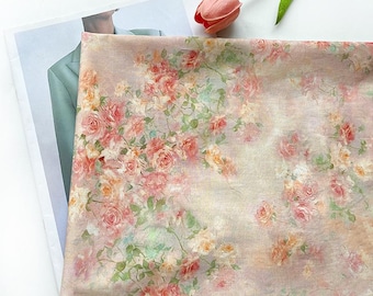 May include: A floral fabric with a pattern of pink, peach, and yellow roses and green leaves. The roses are clustered, creating a romantic, vintage aesthetic. The fabric is draped, with a pink tulip in the upper right corner. The fabric is likely for dressmaking.