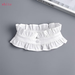 May include: A white, ruffled collar with a button closure. The collar is made of a soft fabric and features a layered, frilled design. The word "white" is in the top left corner.