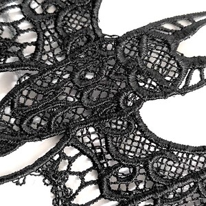 May include: Close-up of a black lace mask with detailed floral and geometric patterns. The delicate, openwork design features a combination of curved and straight lines, creating a visually appealing texture. The mask is likely for a costume or special occasion.