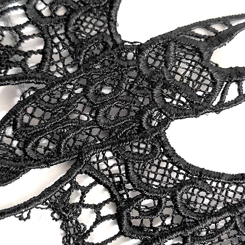 May include: Close-up of a black lace mask with detailed floral and geometric patterns. The delicate, openwork design features a combination of curved and straight lines, creating a visually appealing texture. The mask is likely for a costume or special occasion.