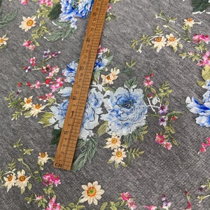 Puede incluir: Tela de tul gris con un patr&oacute;n floral con flores azules, rosas y amarillas. La tela se mide con una regla en pulgadas.