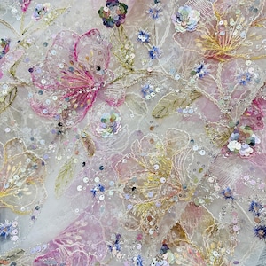 May include: Close-up of a delicate fabric with floral embroidery. The design features pink, yellow, and blue flowers with green leaves, all embellished with sequins. The fabric has a sheer, lacy appearance, creating a romantic and elegant aesthetic.