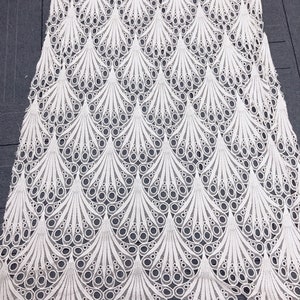 May include: White lace fabric with a repeating pattern of stylized peacock feathers. The delicate design features openwork circles and curved lines, creating a textured, airy appearance. The fabric is likely used for apparel or decorative purposes.