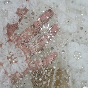 以下が含まれることがあります： 白いチュール生地に、3Dの花のアップリケとパールとスパンコールの装飾が施されています。