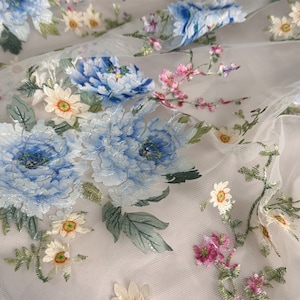 Puede incluir: Tela de tul blanco con flores bordadas en azul, rosa y amarillo. Las flores est&aacute;n en un patr&oacute;n floral y tienen un efecto 3D.