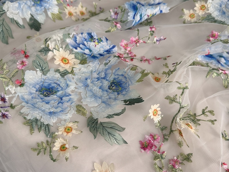 Puede incluir: Tela de tul blanco con flores bordadas en azul, rosa y amarillo. Las flores est&aacute;n en un patr&oacute;n floral y tienen un efecto 3D.