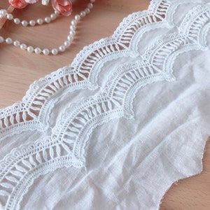 May include: White cotton lace trim with a scalloped edge and a delicate floral pattern. The lace is approximately 2.5 cm wide.