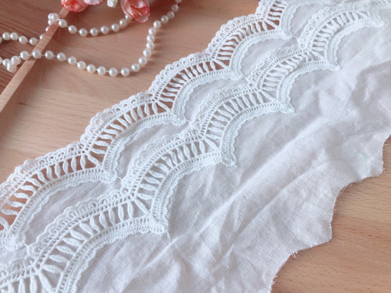 May include: White cotton lace trim with a scalloped edge and a delicate floral pattern. The lace is approximately 2.5 cm wide.