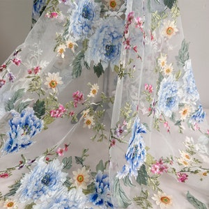 Puede incluir: Tela blanca transparente con un patr&oacute;n floral bordado. Las flores son azules, rosas y amarillas. La tela es delicada y tiene una textura suave.