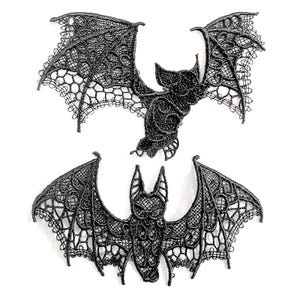 May include: Two black lace bat appliqu&eacute;s. One bat is in flight, the other is shown with its wings spread. The bats have detailed wing patterns and are set against a white background. These appliqu&eacute;s are ideal for Halloween or gothic-themed crafts.