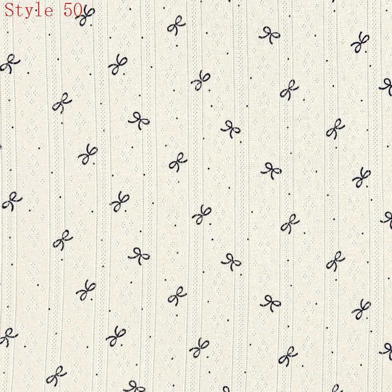 May include: An off-white fabric featuring a repeating pattern of small black bows and tiny dots, organized in vertical columns with subtle ribbed textures. The top left corner displays the red text Style 50.