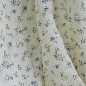 May include: White fabric with a small, delicate floral pattern in shades of blue and pink.