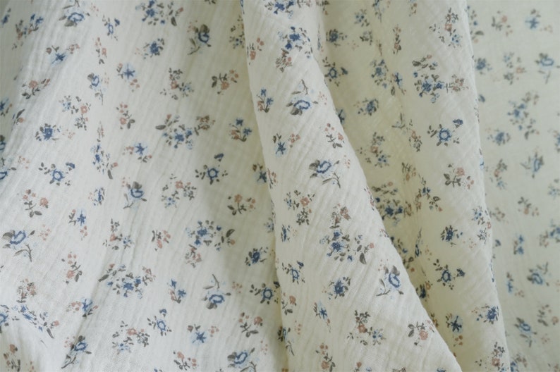 May include: White fabric with a small, delicate floral pattern in shades of blue and pink.