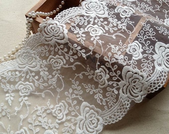 May include: White floral lace trim with a delicate pattern of flowers and leaves. The lace is sheer and has a soft, romantic feel.