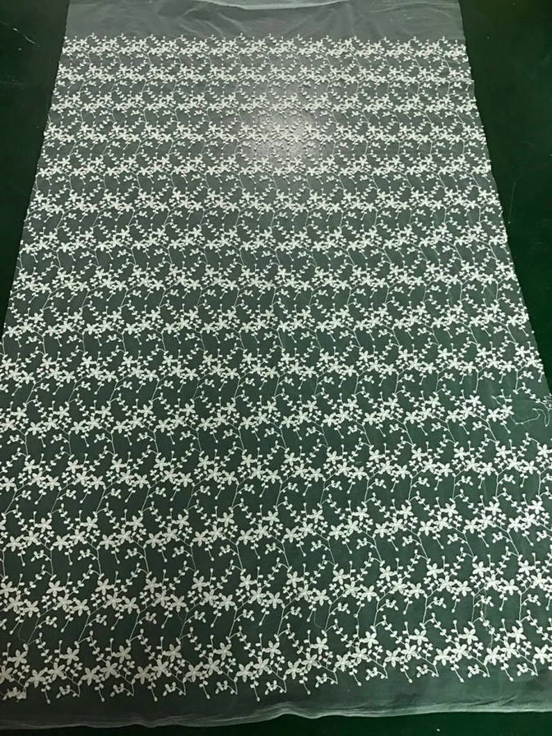 K&ouml;nnte beinhalten: Wei&szlig;er, gestickter Blumenspitzenstoff mit einem zarten Muster aus kleinen wei&szlig;en Bl&uuml;ten und Ranken auf einem durchsichtigen Netzstoff.