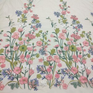 May include: A floral embroidered fabric with pink, white, and blue flowers on a cream background.