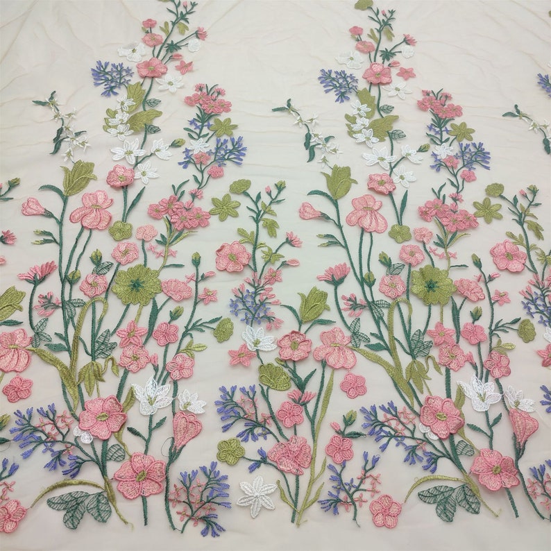May include: A floral embroidered fabric with pink, white, and blue flowers on a cream background.