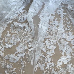 May include: White floral lace fabric with a delicate pattern of flowers and leaves. The lace is embellished with sequins, adding a touch of sparkle.