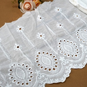 May include: White cotton lace trim with a scalloped edge and delicate floral embroidery. The lace has a repeating pattern of small flowers and larger, openwork designs.