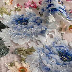 Puede incluir: Tela blanca transparente con flores bordadas azules y verdes. Las flores son en relieve y tienen un efecto 3D.