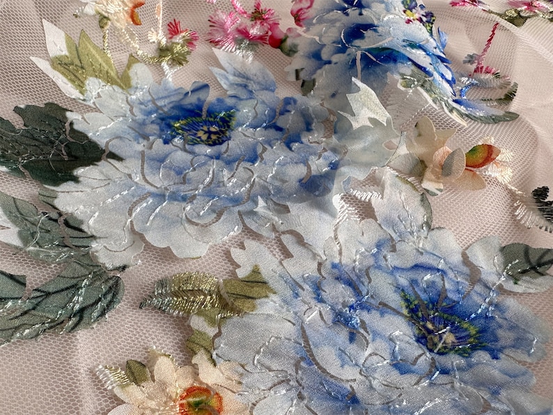 Puede incluir: Tela blanca transparente con flores bordadas azules y verdes. Las flores son en relieve y tienen un efecto 3D.